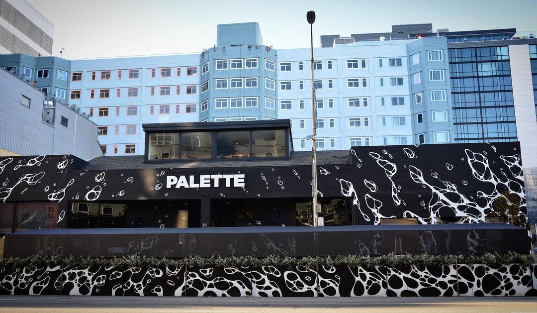 Palette: A short, wide building pained black with white designs; a tall blue apartment building is in the background.