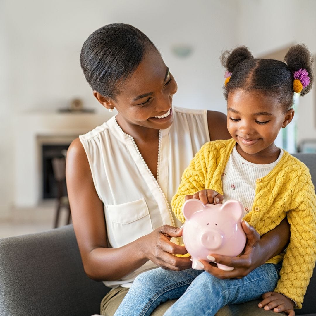 Black woman with a Black girl sitting on her lap holding a piggy bank.