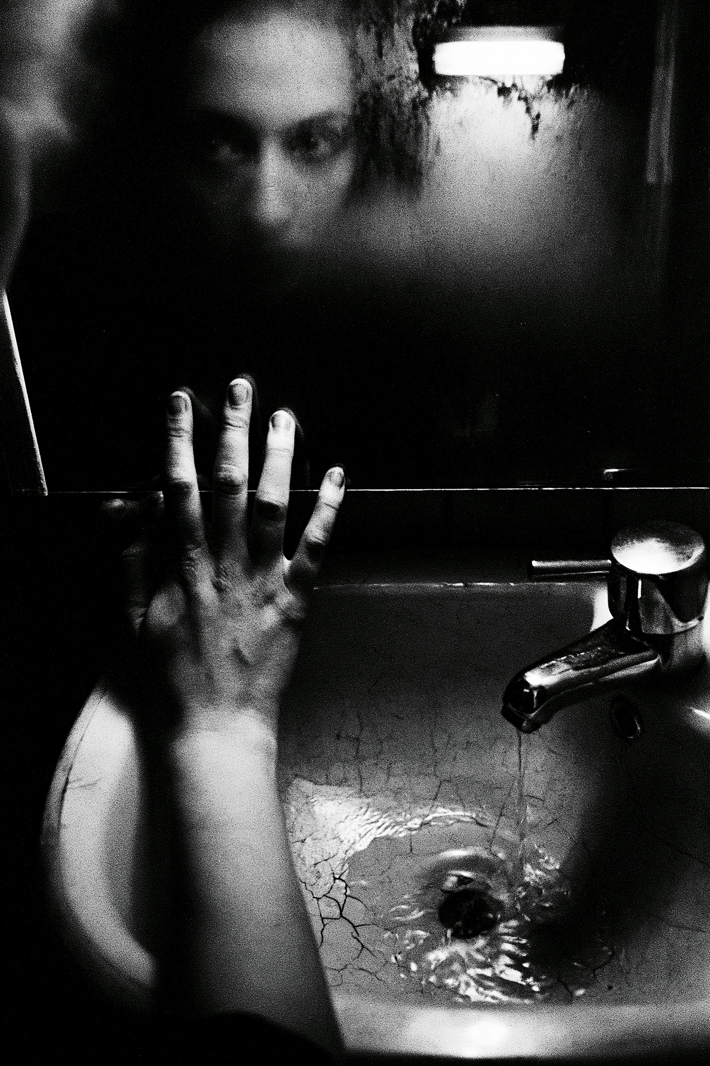 black and white extreme close-up of a woman’s hands gripping a chipped enamel sink basin in a dark Scandinavian bathroom, her face barely visible in the fogged mirror above, 35mm Ilford HP5 pushed to 1600, single fluorescent tube flickering overhead casting green-tinted hard light, water droplets on chrome tap and cracked ceramic, crushed blacks and coarse grain with heavy vignetting — ar 3:4 — raw — stylize 80 — v 8.1