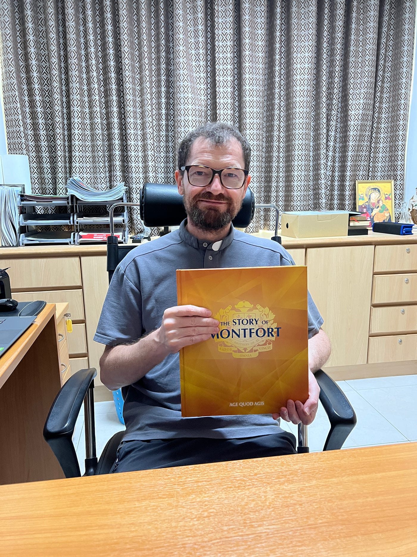 Fr Dominique with the Montfort School’s coffeetable book commemorating its centenary in 2016