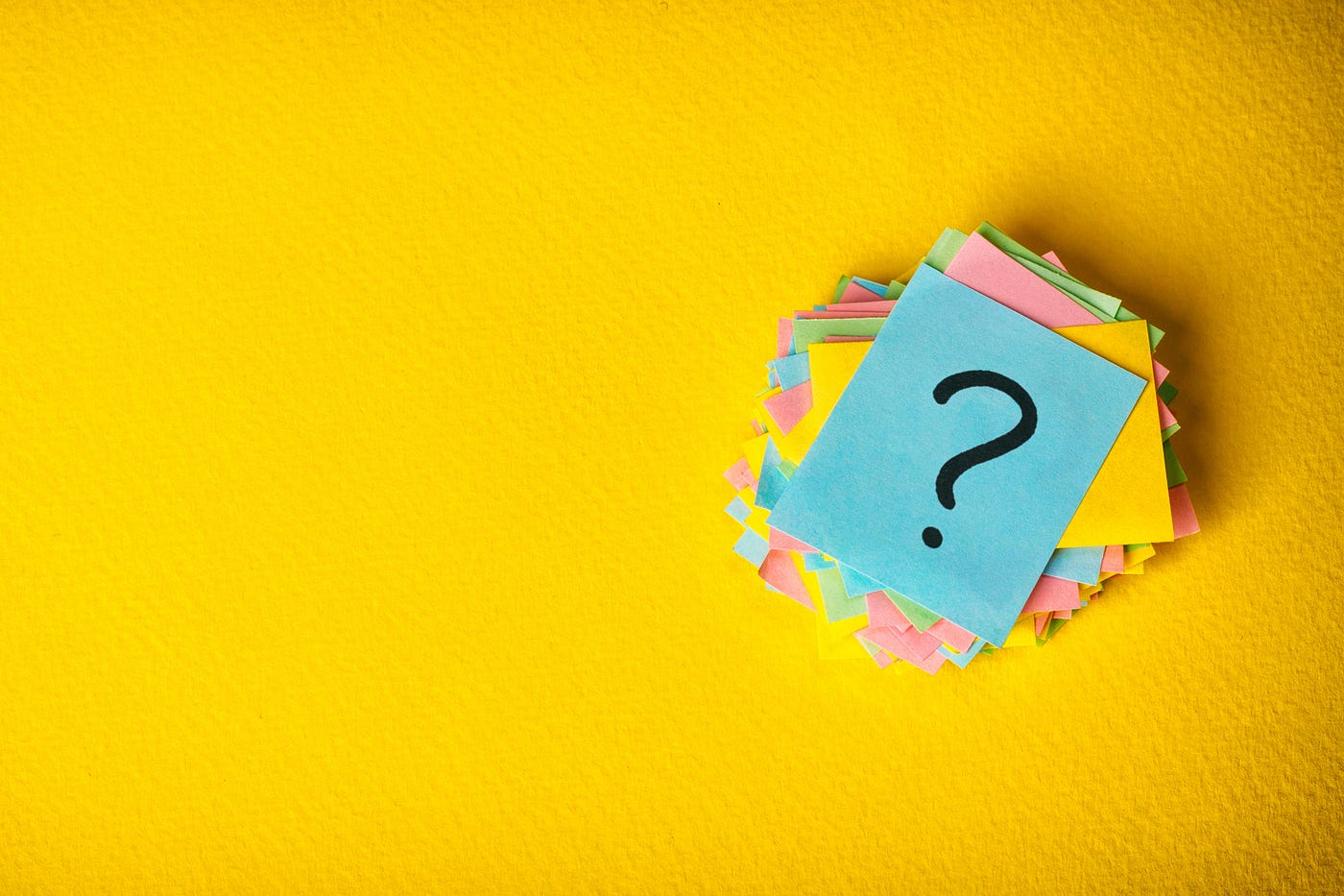 A stack of pastel colored squares on a yellow background with a black question mark drawn on the topmost page