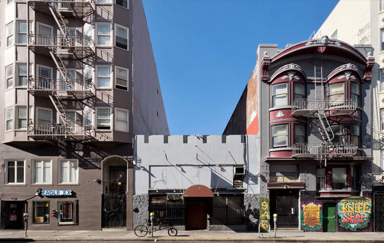 A shot of a short building flanked by taller, San Francisco-style houses.