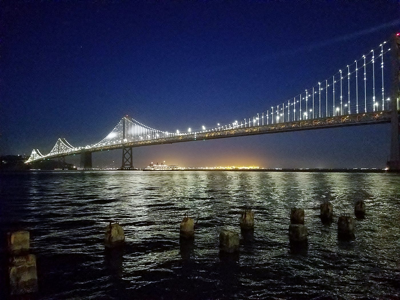 The east span of the Bay Bridge at night, as seen from the East Bay. Its cables are illuminated.