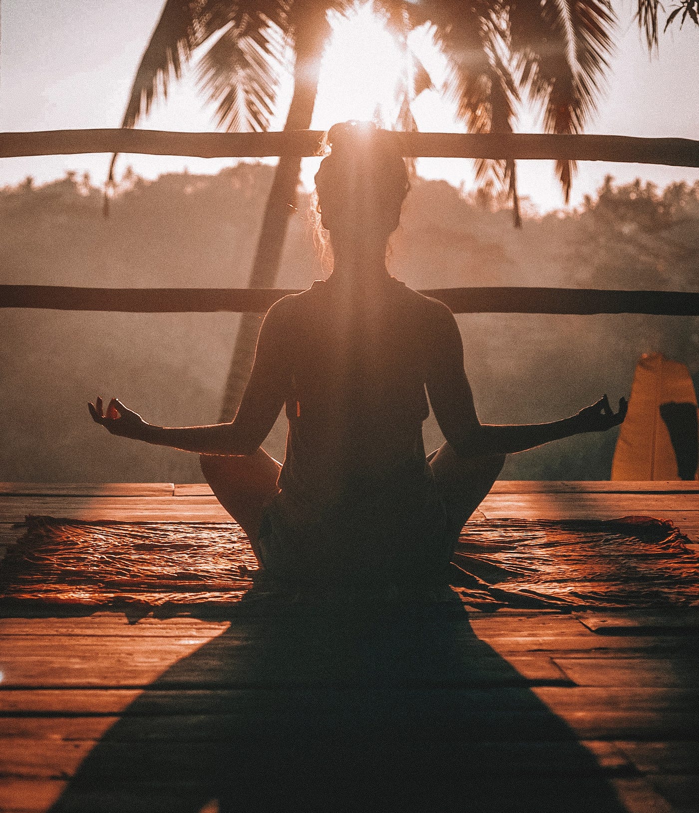 A woman sits in the sun in a meditative pose on a wooden deck.