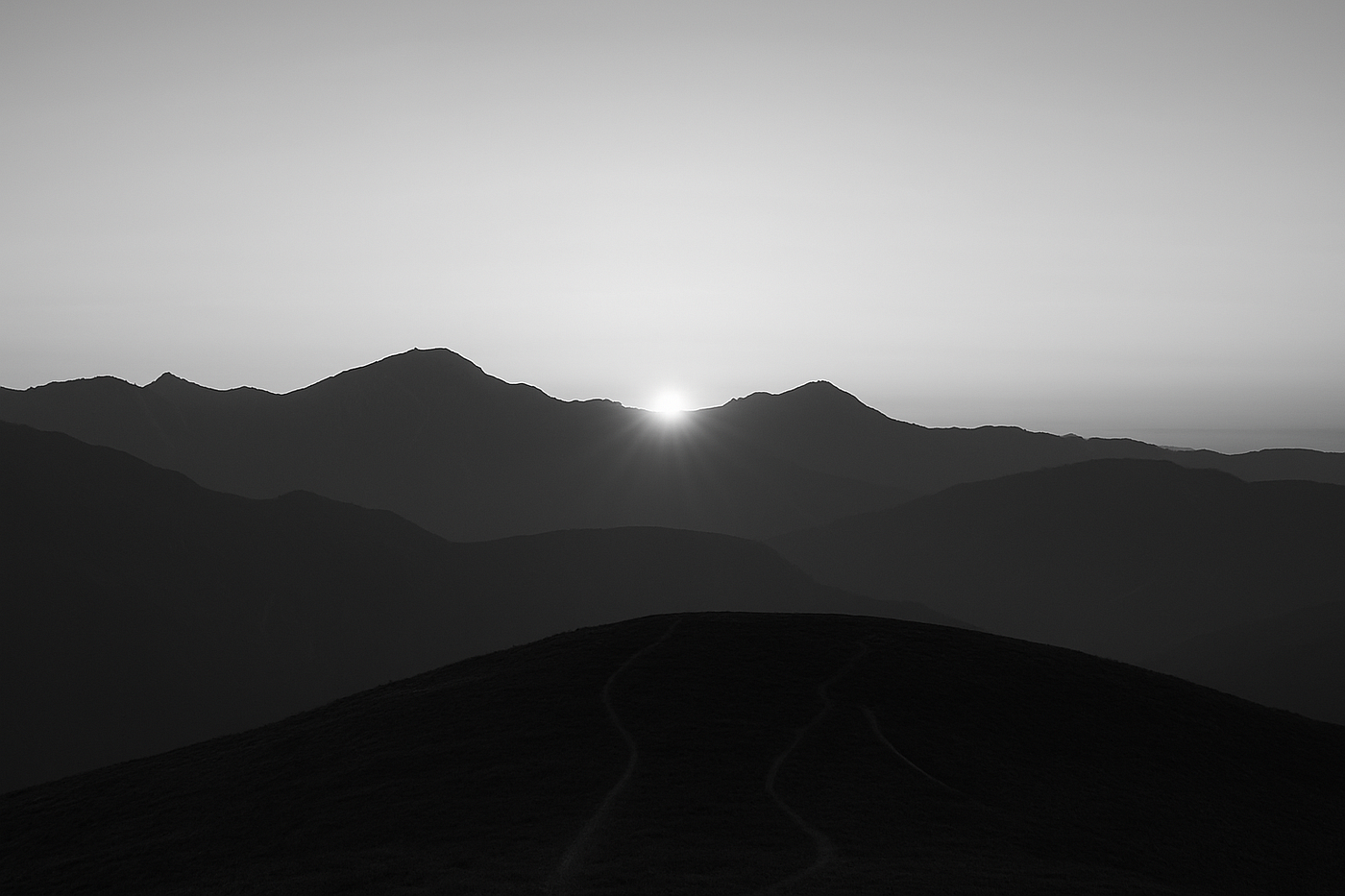 일몰 무렵의 산봉우리를 담은 흑백 사진으로, 희미한 세 개의 산길이 위로 이어지며, 좋은 삶으로 이어지는 다양한 길이 지평선을 향해 모이는 모습을 상징합니다.<BR>