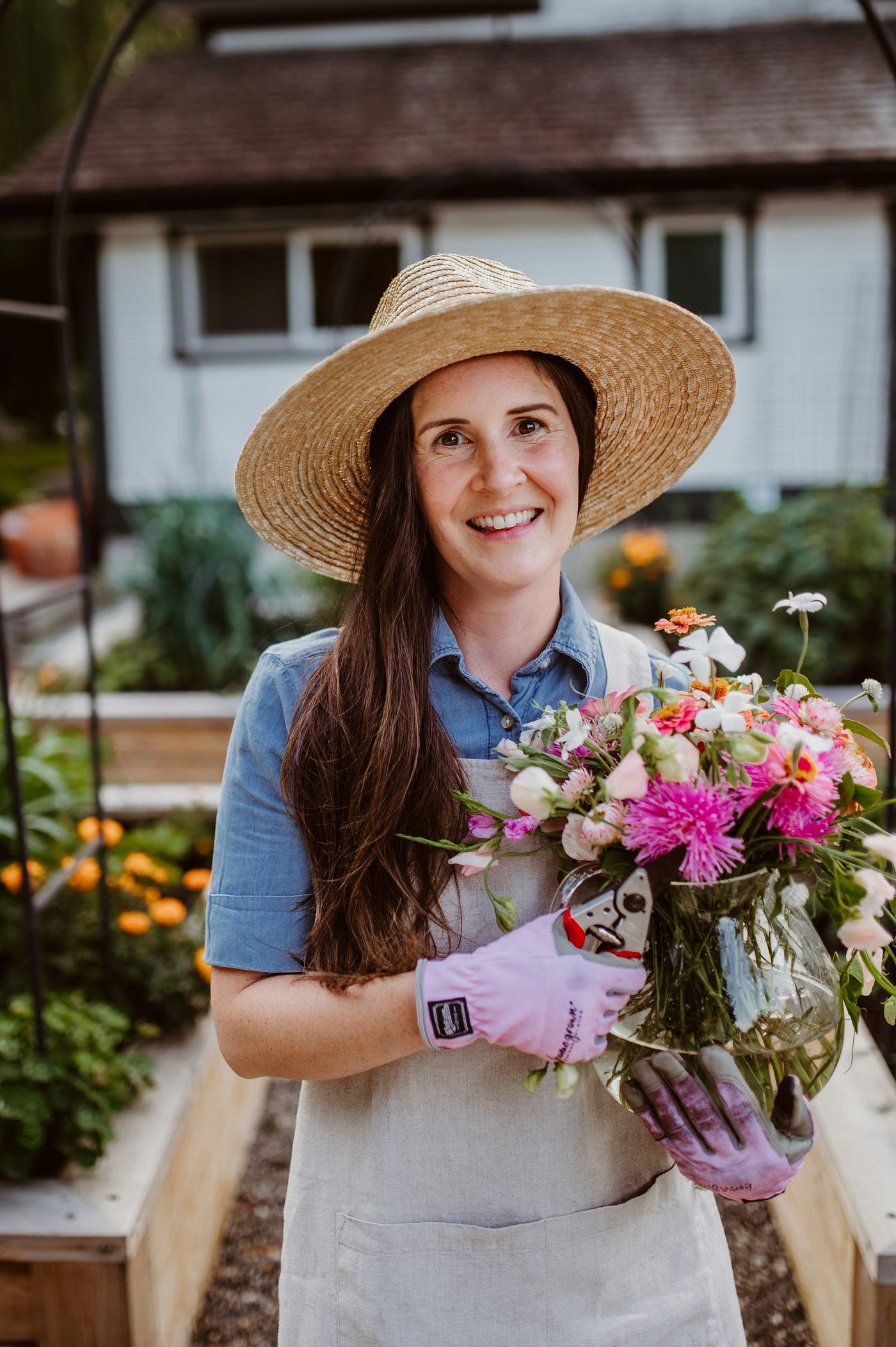 A woman wearing a linen apron in her backyard garden holding flower from the garden. source ai generated