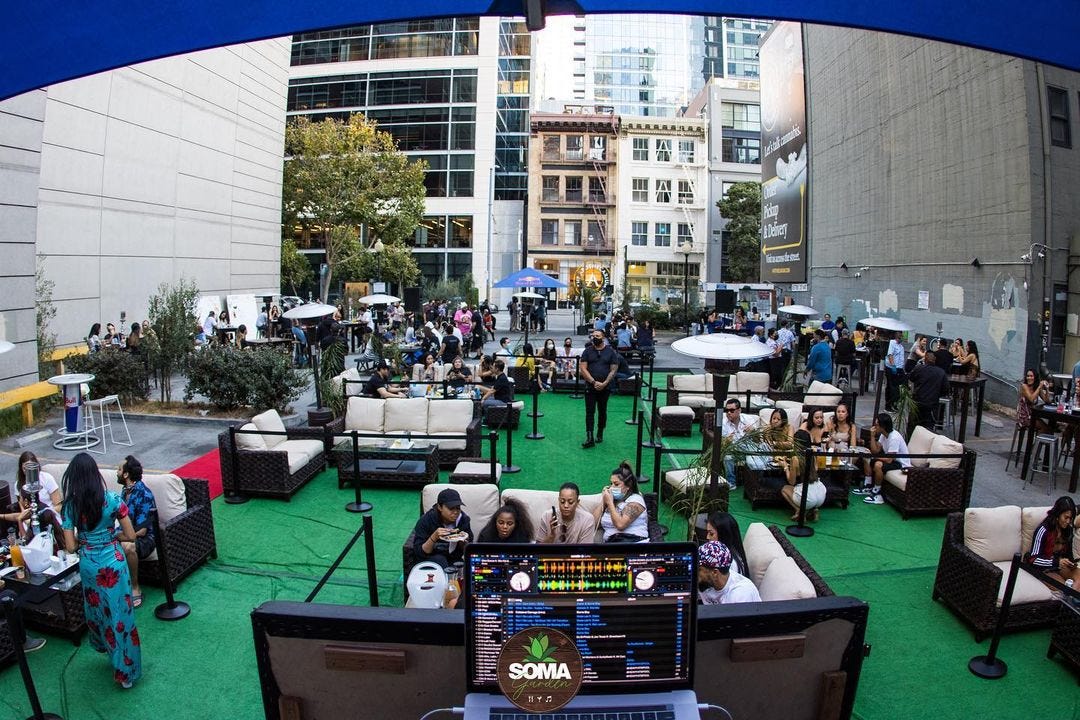 An outdoor event space between two city buildings with people sitting in socially distanced booths.