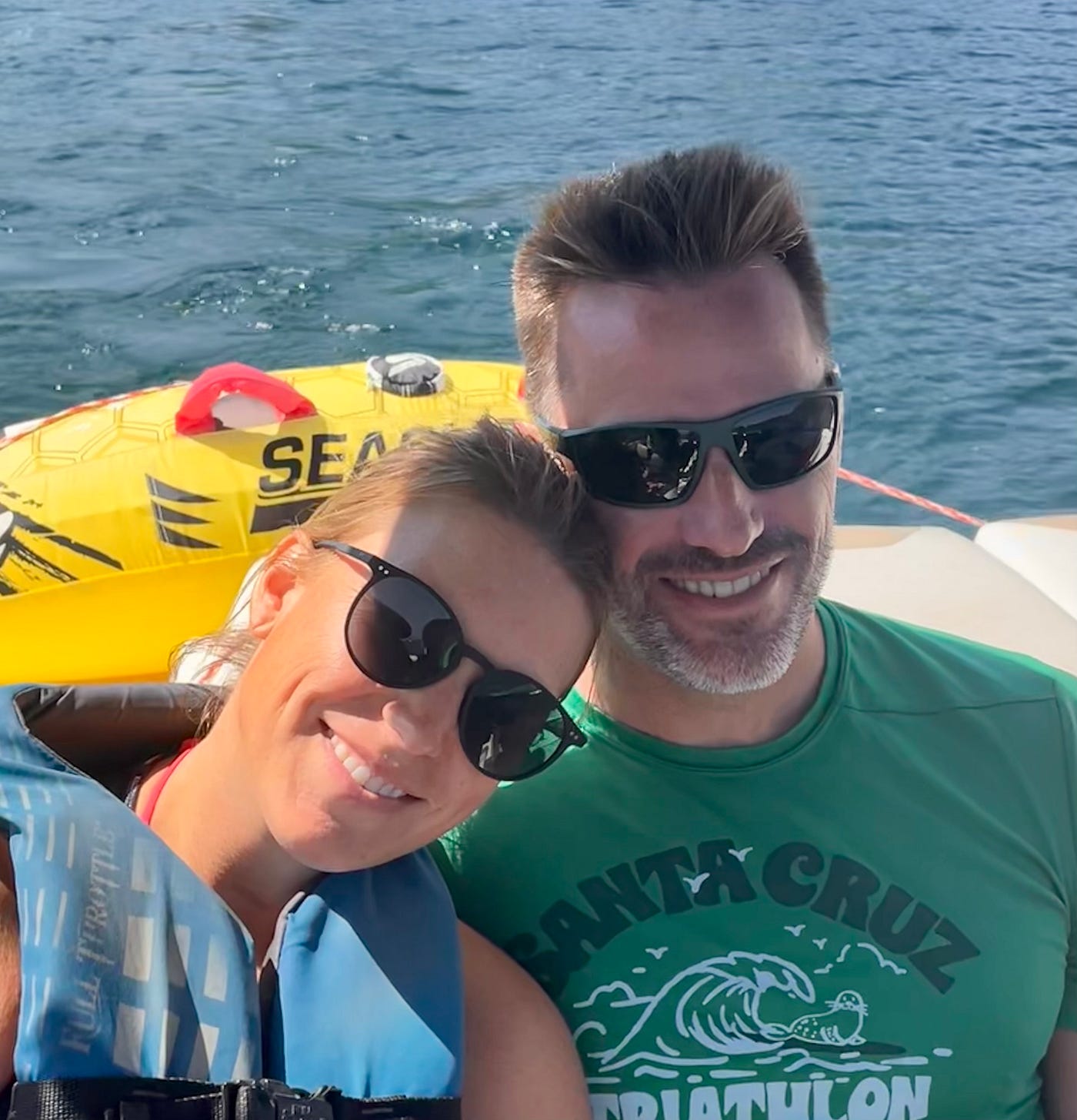 선글라스를 쓴 남녀가 쾌속정 뒷좌석에 나란히 앉아 서로 머리를 기댄 채 서 있다.<BR> 배경에는 밝은 노란색 튜브가 보이는데, 푸른 물에 반쯤 떠 있다.<BR>