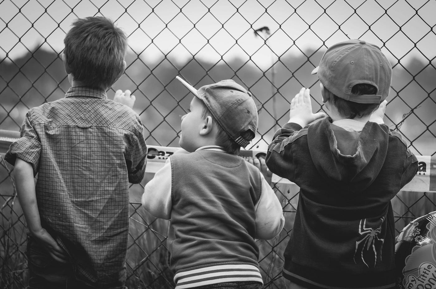 Three boys facing a fence, watching a game | Photo by Pixabay via Pexels