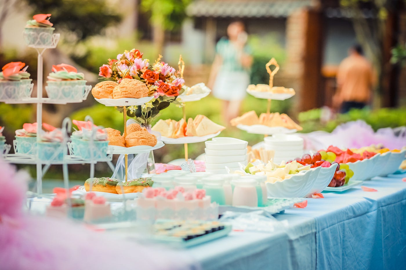 A table in a garden filled with various colourful fruits and cupcakes on dainty cake stands.