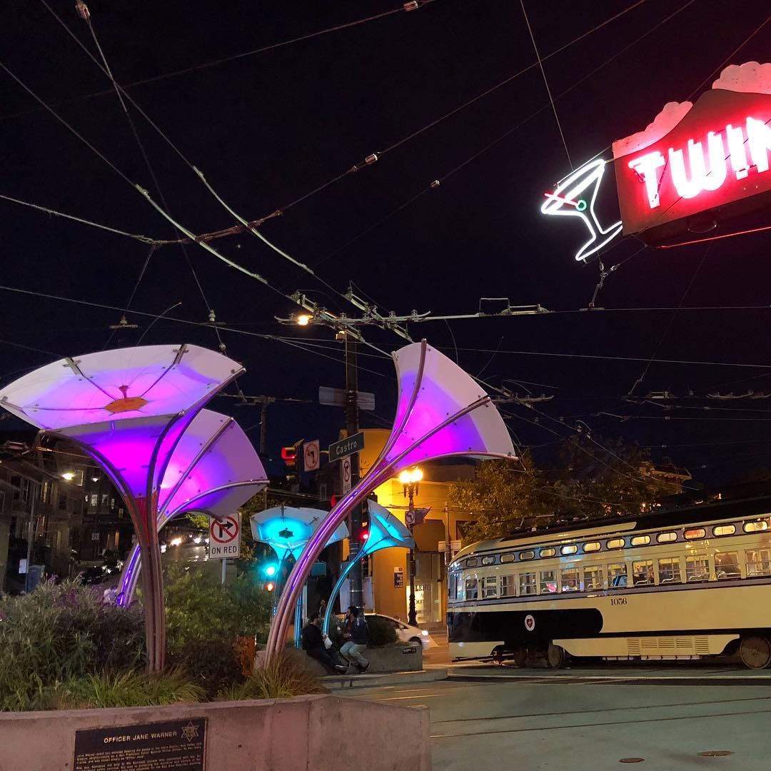 Illuminated purple structures that look like the cone part of gramophones, seen with a streetcar in the background.