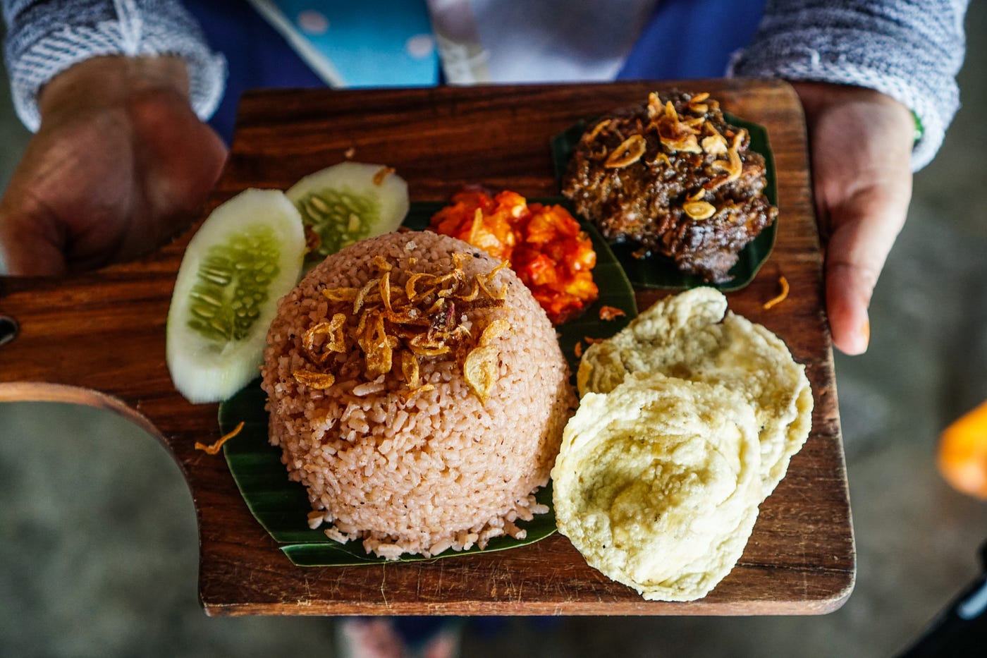 Sepiring nasi minyak yang harum dengan taburan kacang mete dan kismis, disajikan dengan irisan daging kambing dan acar segar