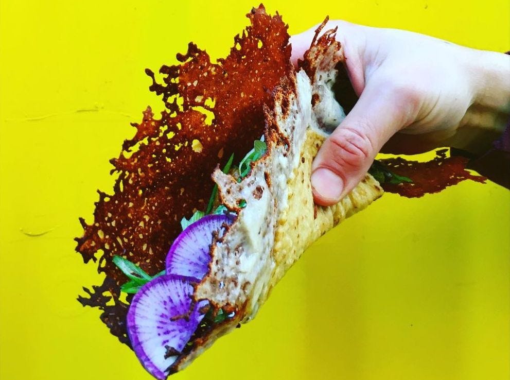 Hand holding a taco made of a lacy, super-thin tortilla.