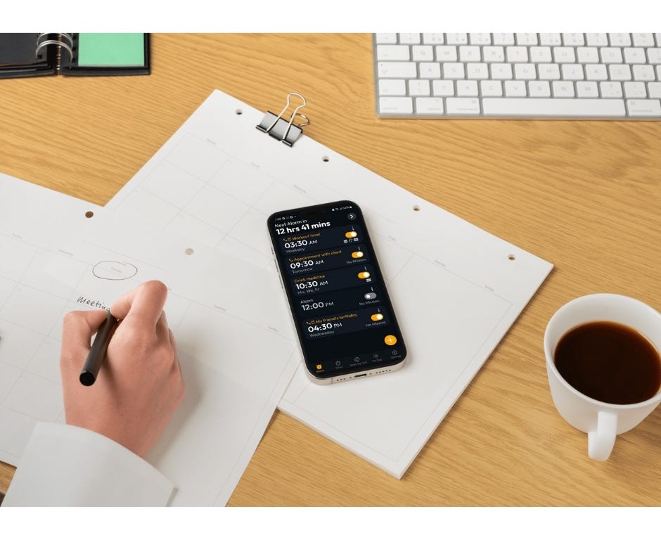 Smartphone displaying a schedule on an alarm app placed on a workspace desk with a calendar, coffee cup, and keyboard in the background. Ideal for blogs about productivity, time management, and the best alarm apps. Keywords: safe alarm clock, best alarm app, free alarm clock app, daily reminders, time management.