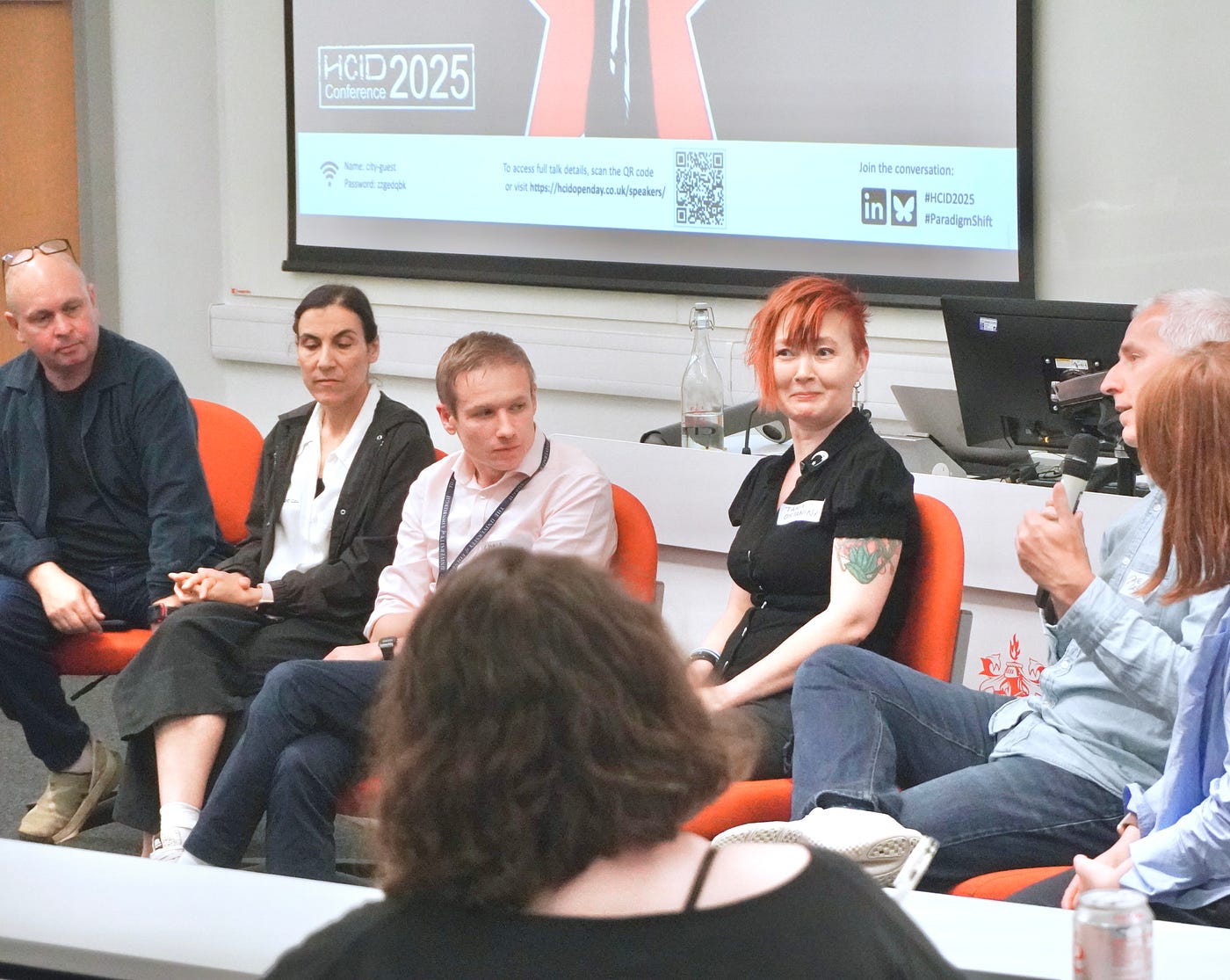 A photo of a panel of several speakers, including the author, in front of an audience.