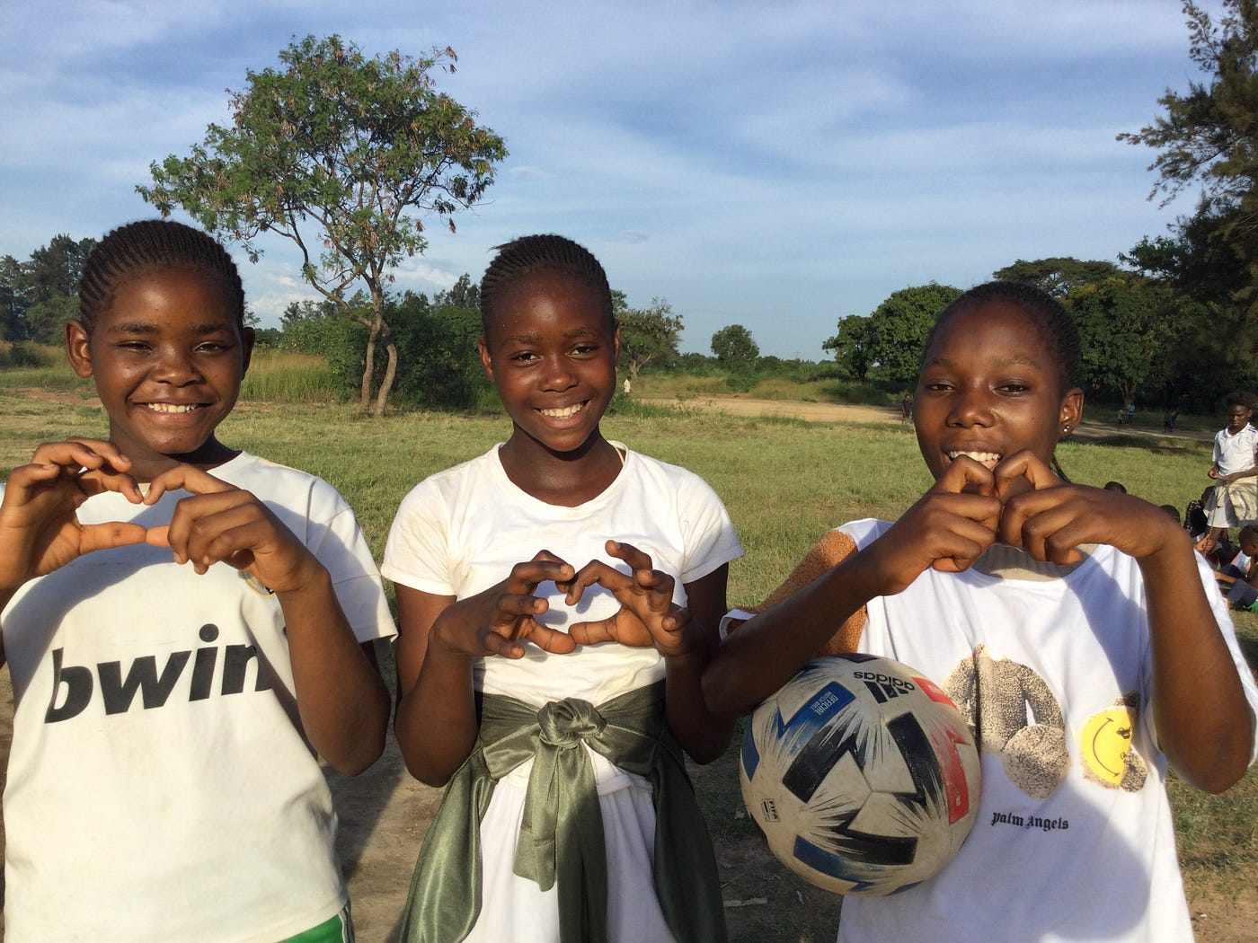 Three young people holding up hand hearts and wearing white jerseys.