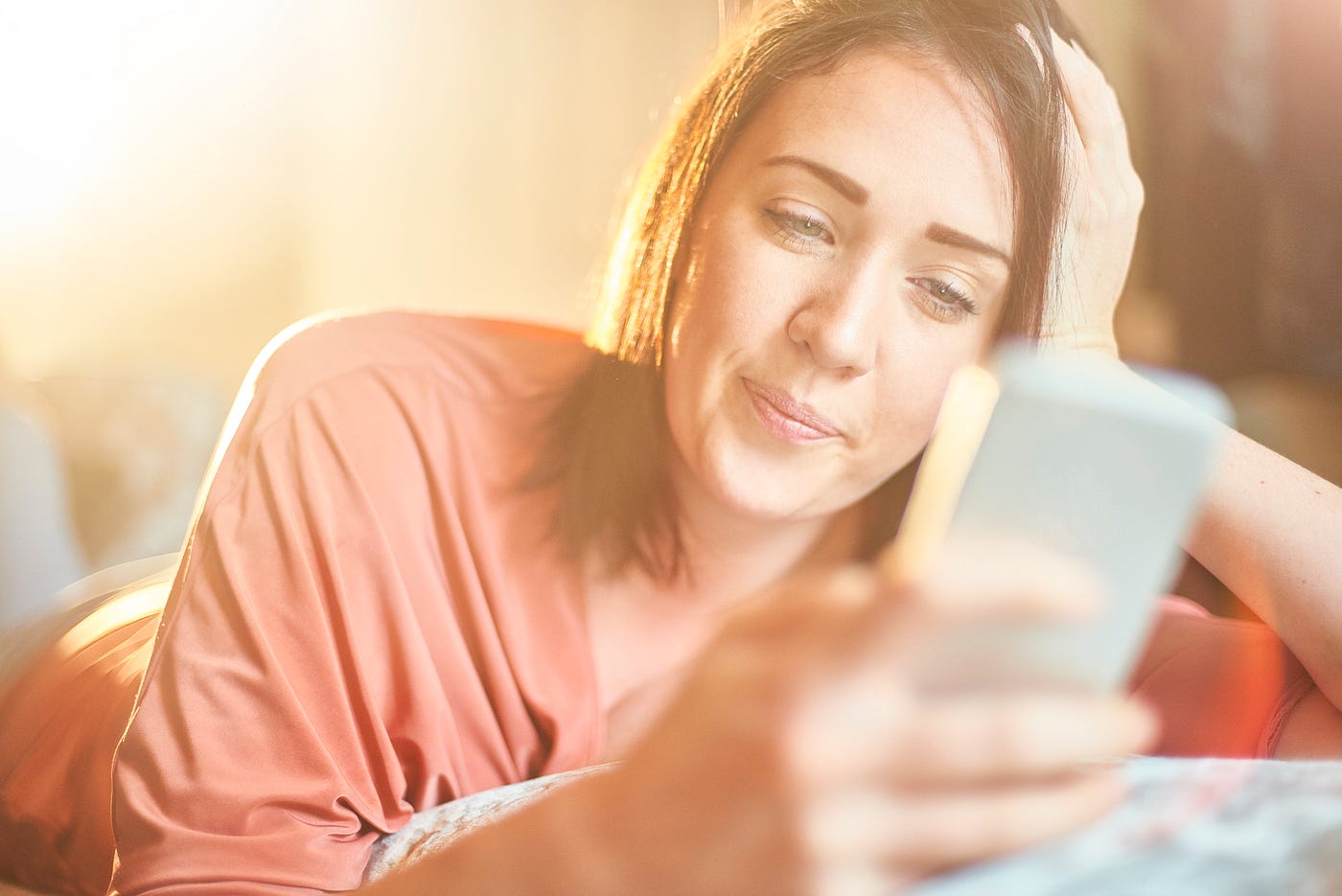 A young woman lying on a sofa looking through an online dating app.