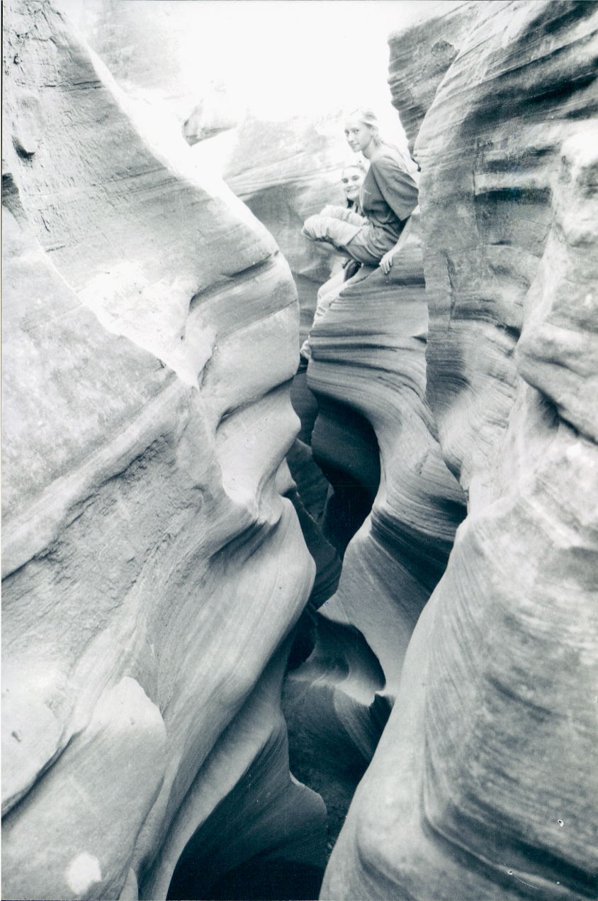 Two high school aged girls sitting on top of a narrow slot canyon smiling.