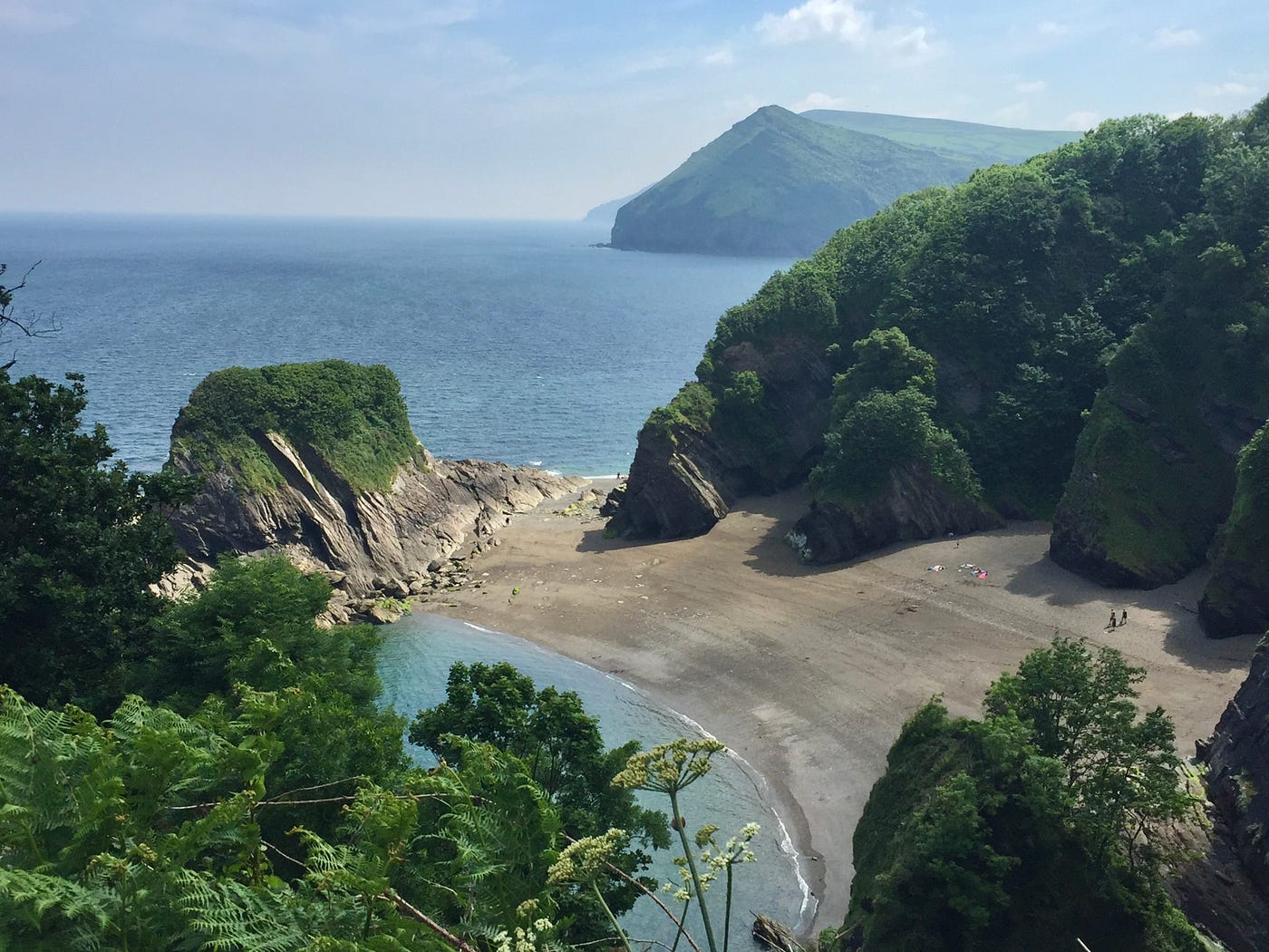 A coastal view looking down upon a curving sandy cove with wooded headlands.