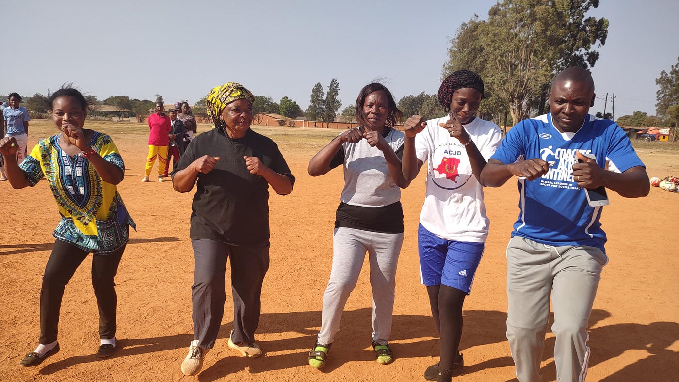 A group of participants on a dirt field, engaging in physical activity and moving their bodies.