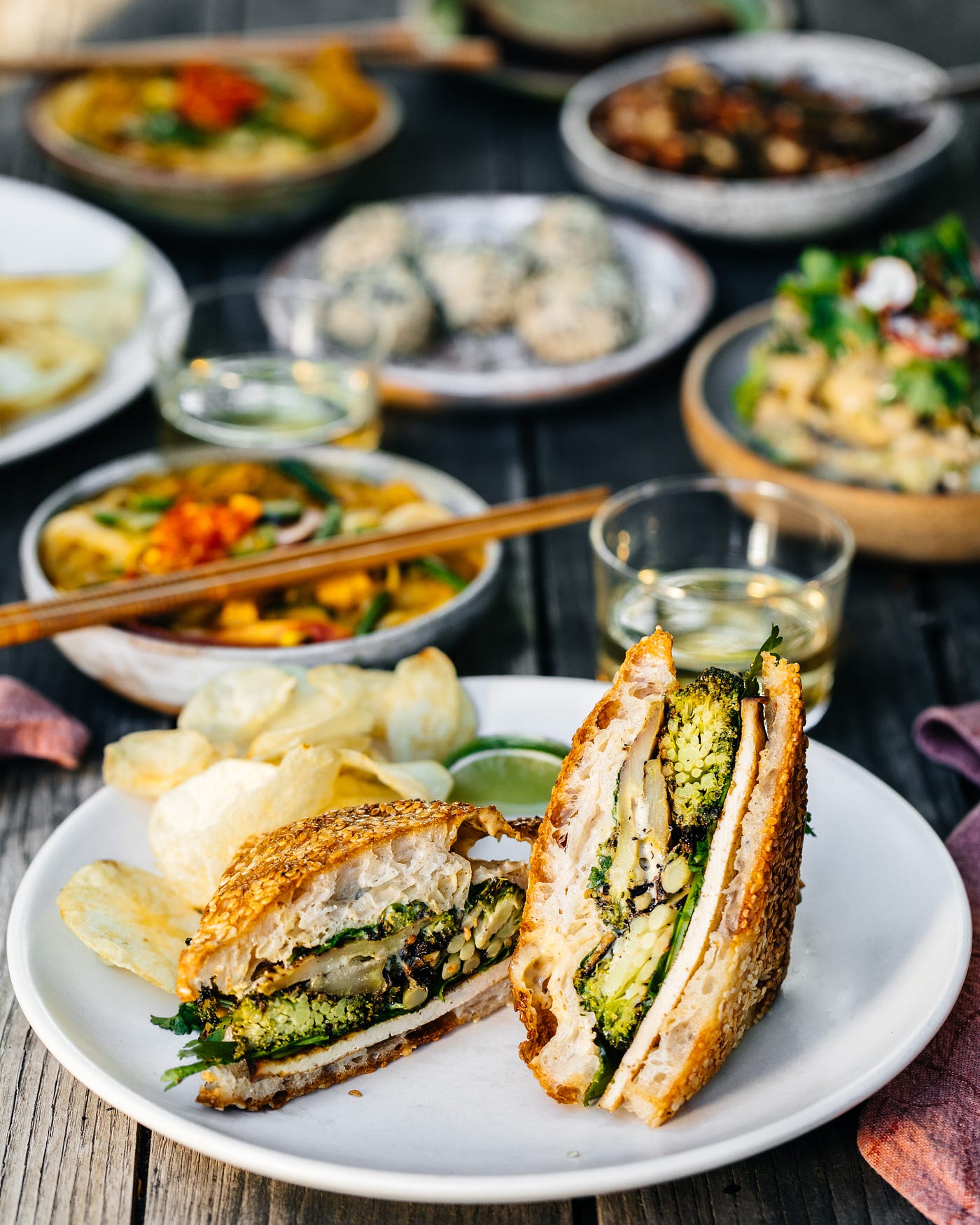 A spread of different dishes on a dining table, with a grilled sandwich closest to the viewer.