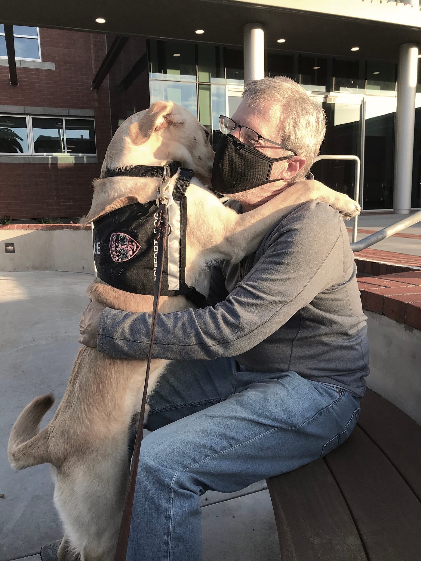 Paul, wearing a mask, hugs the police dog in an outdoor setting.