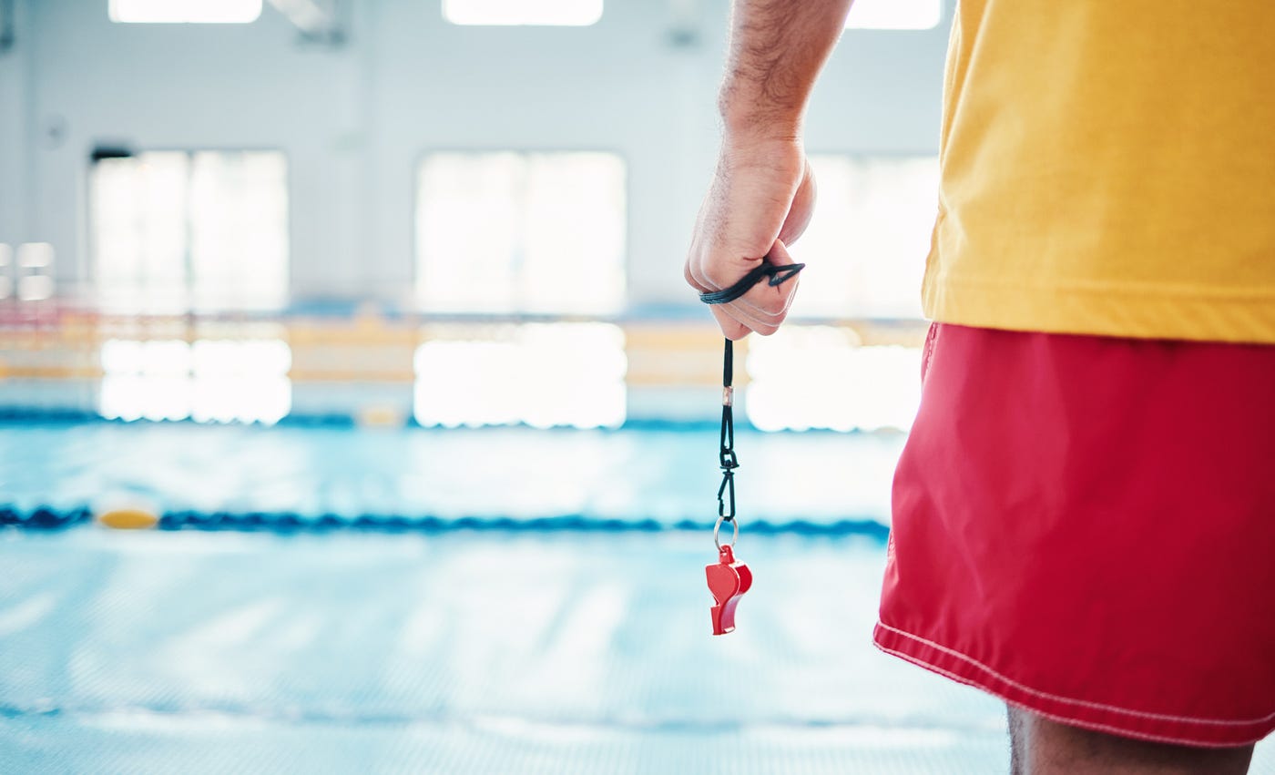 “ Hands, lifeguard and whistle by swimming pool for water safety, security or ready for rescue indoors. Hand of expert swimmer holding signal tool for warning, safe swim or responsibility for awareness “ | by PeopleImages | Shutterstock