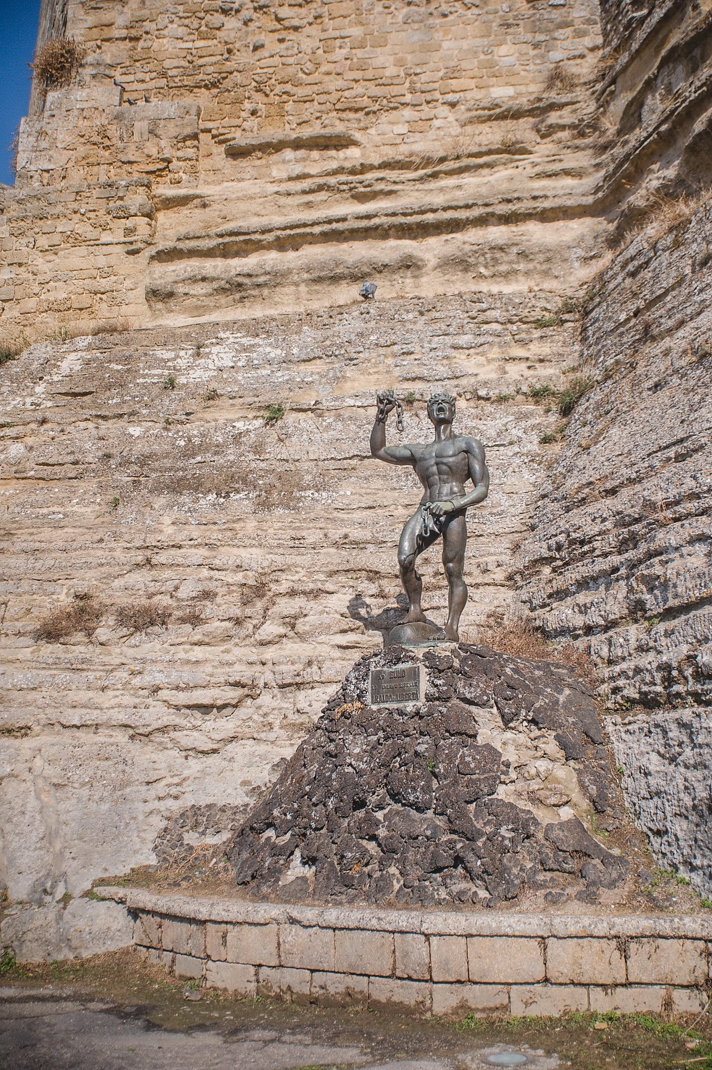 High on the plateau of Enna, beneath the looming shadow of Castello di Lombardia, a statue stands —…