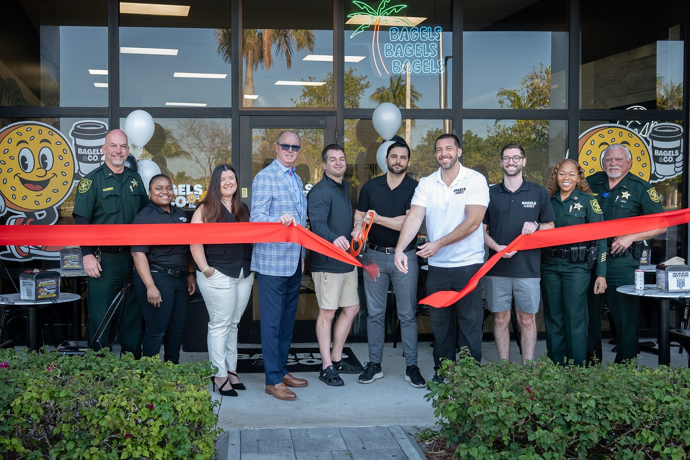 (left to right) Natasha Nash, Georgina Cavendish, Broward County Commissioner Lamar Fisher, David Kaplan, Mike Marsh, Matthew Driscoll, Mark Kaplan and officers from Broward County Sheriff’s Office cut the ribbon at the Bagels & Co. in Pompano Beach. (Credit: Michael Murphy)