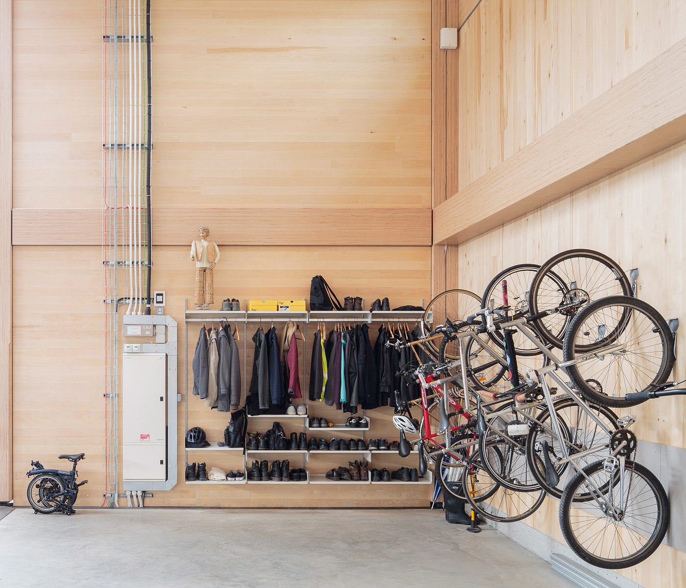 Vitsoe co-working space. There is a customized rack holding shoes, jackets and other accessories next to an electric circuit board with wires streaking up the wall. There is also an improvised bike rack with bikes hanging from the wall. The walls are made completely of wood. Photo by Dirk Linder.