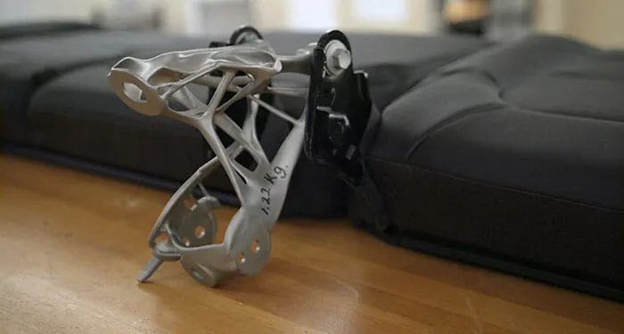 New seat belt bracket designed by human designers working with improved AI tools, replacing an eight-part assembly with a single part that is 40 percent lighter and 20 percent stronger (GM working with Autodesk’s AI generative design tools)