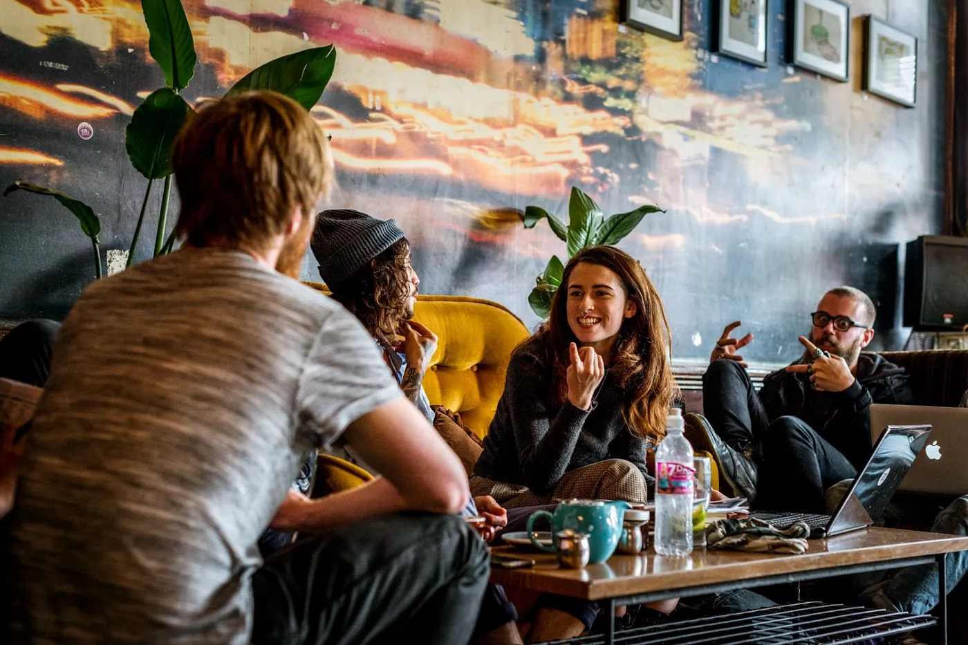 Cover photo of 4 strangers becoming friends in a coffee shop sitting around a coffee table with a variety of drinks on the table.