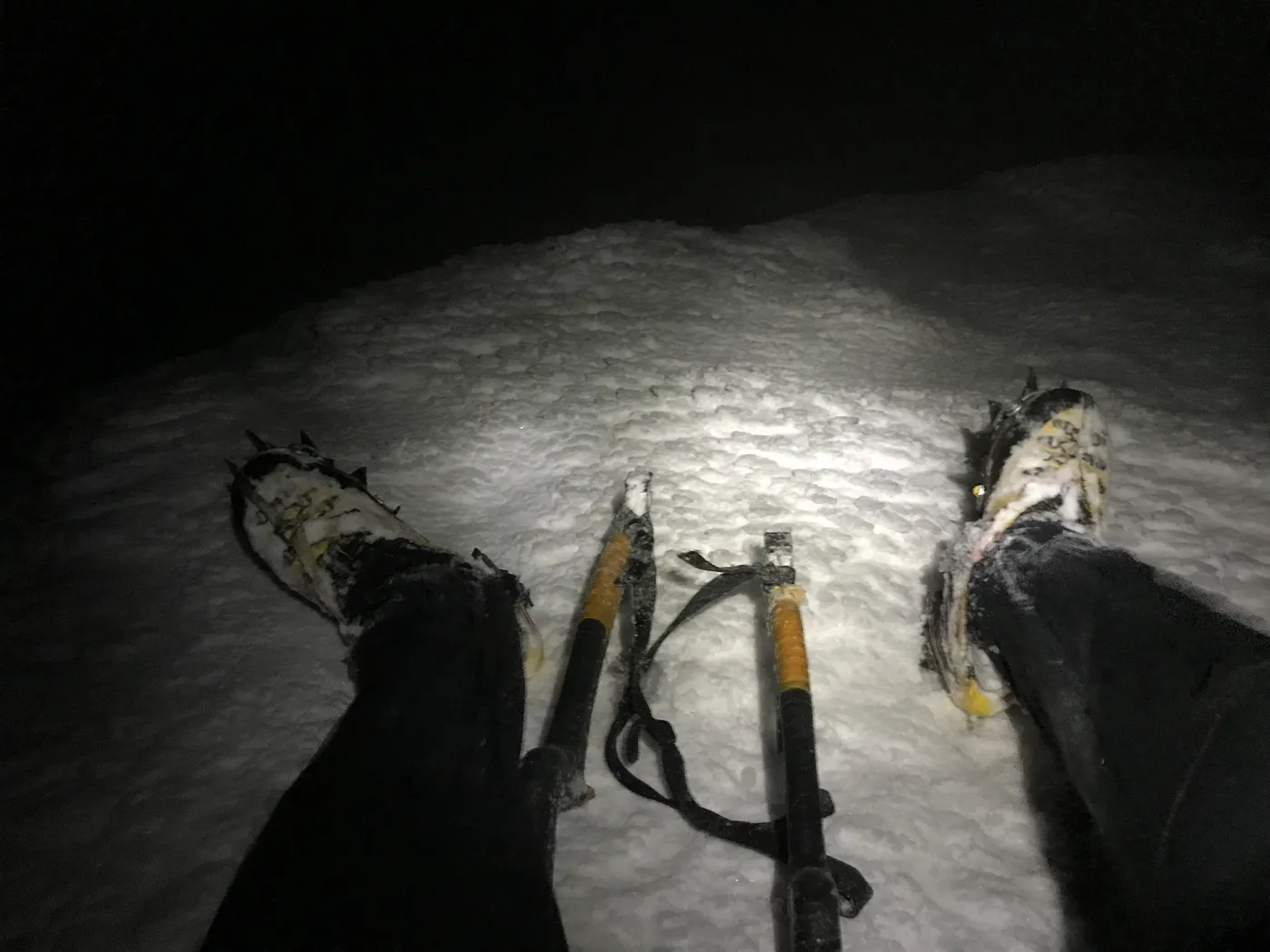 A mountaining stirring a hot drink over small gas stove with an ice climbing tool.