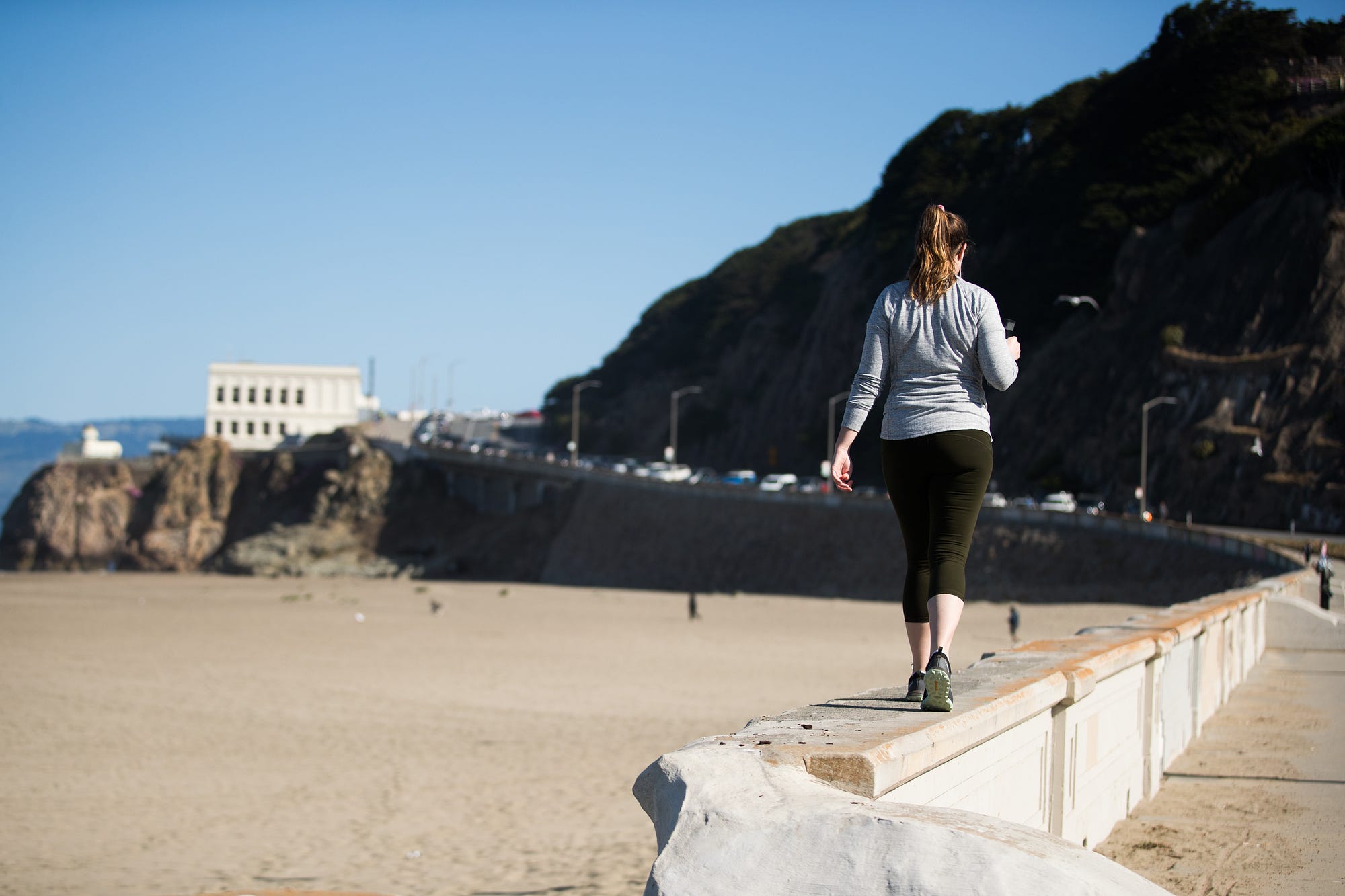 A person walking on concrete barriers on Ocean Beach toward the Cliff House restaurant.
