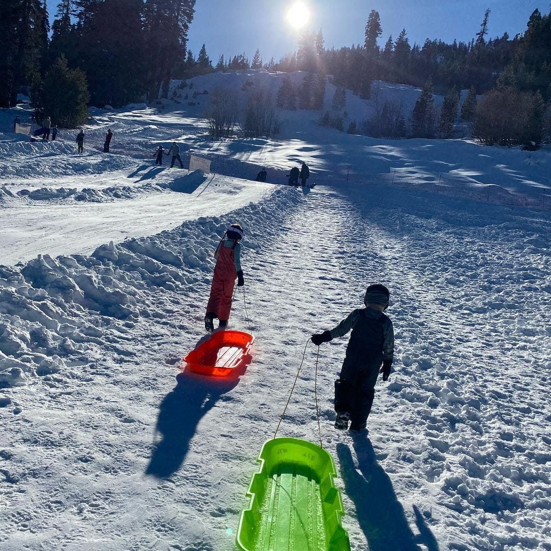 Two children pulling plastic sleds up a gentle, snow-covered slope.