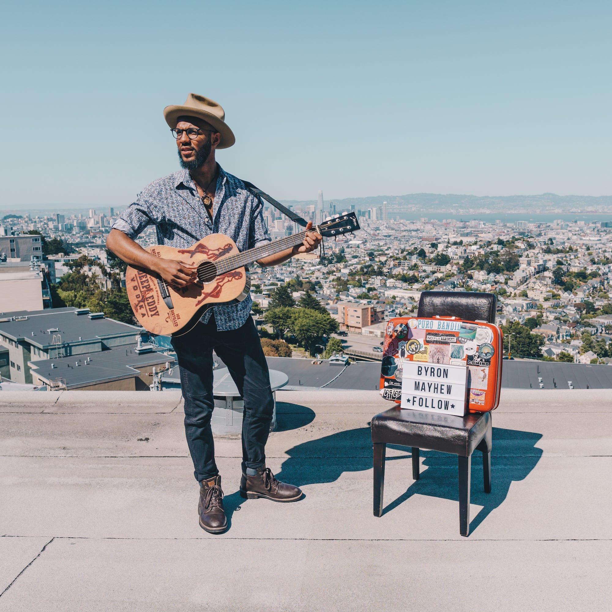 Byron playing guitar while standing on a rooftop, with an expansive view of San Francisco behind him.