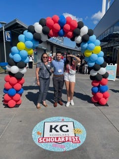 A family poses under a colorful balloon arch at an event.