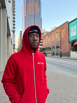Gavin Ayoade wearing a red zip-up hoodie against an urban backdrop.