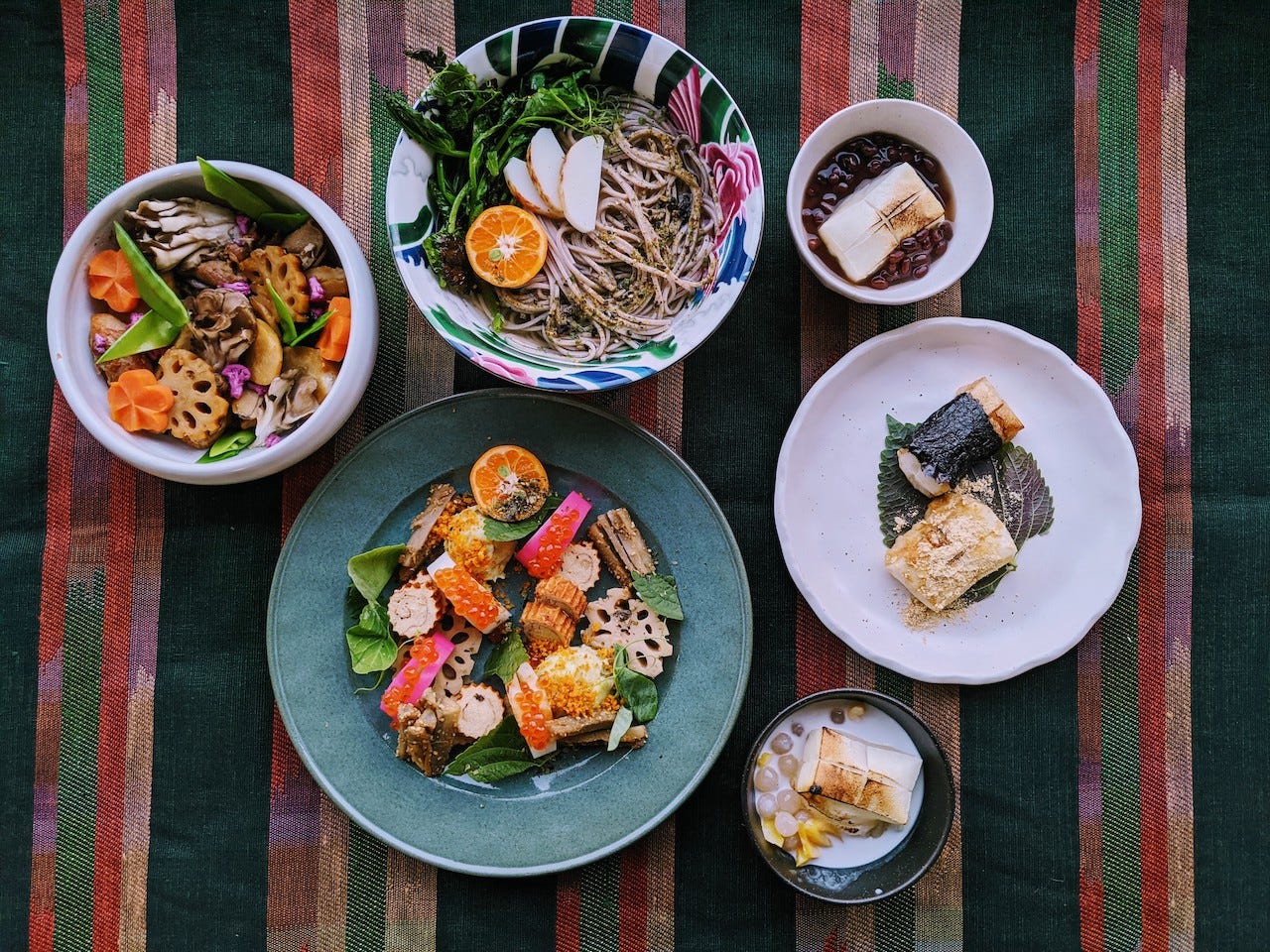 A variety of filipino dishes in ceramic dishes on a tablecloth with vertical green, pink, and rose-colored stripes.