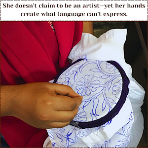 Close-up of a woman’s hand delicately working on a floral hand embroidery design using blue thread on white fabric, held within a purple embroidery hoop. She wears a deep pink dupatta, and the image is overlaid with the quote: “She doesn’t claim to be an artist — yet her hands create what language can’t express.”