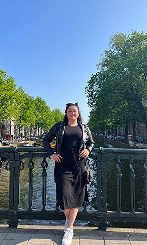 A girl wearing a black dress poses for a photo on a bridge overlooking a canal.