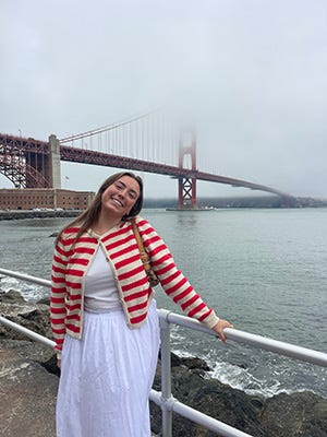 Sofia Bowman stands in front of the Golden Gate Bridge that is partially covered by fog.
