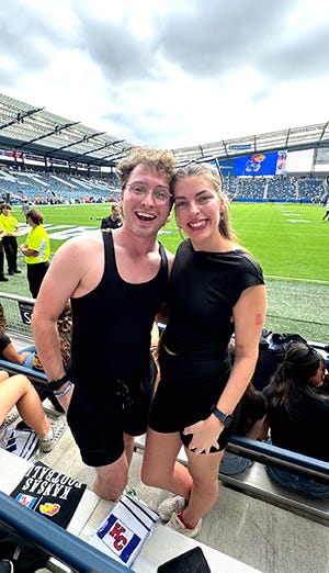 A guy and a girl dressed in black smile while at a KU sporting event.
