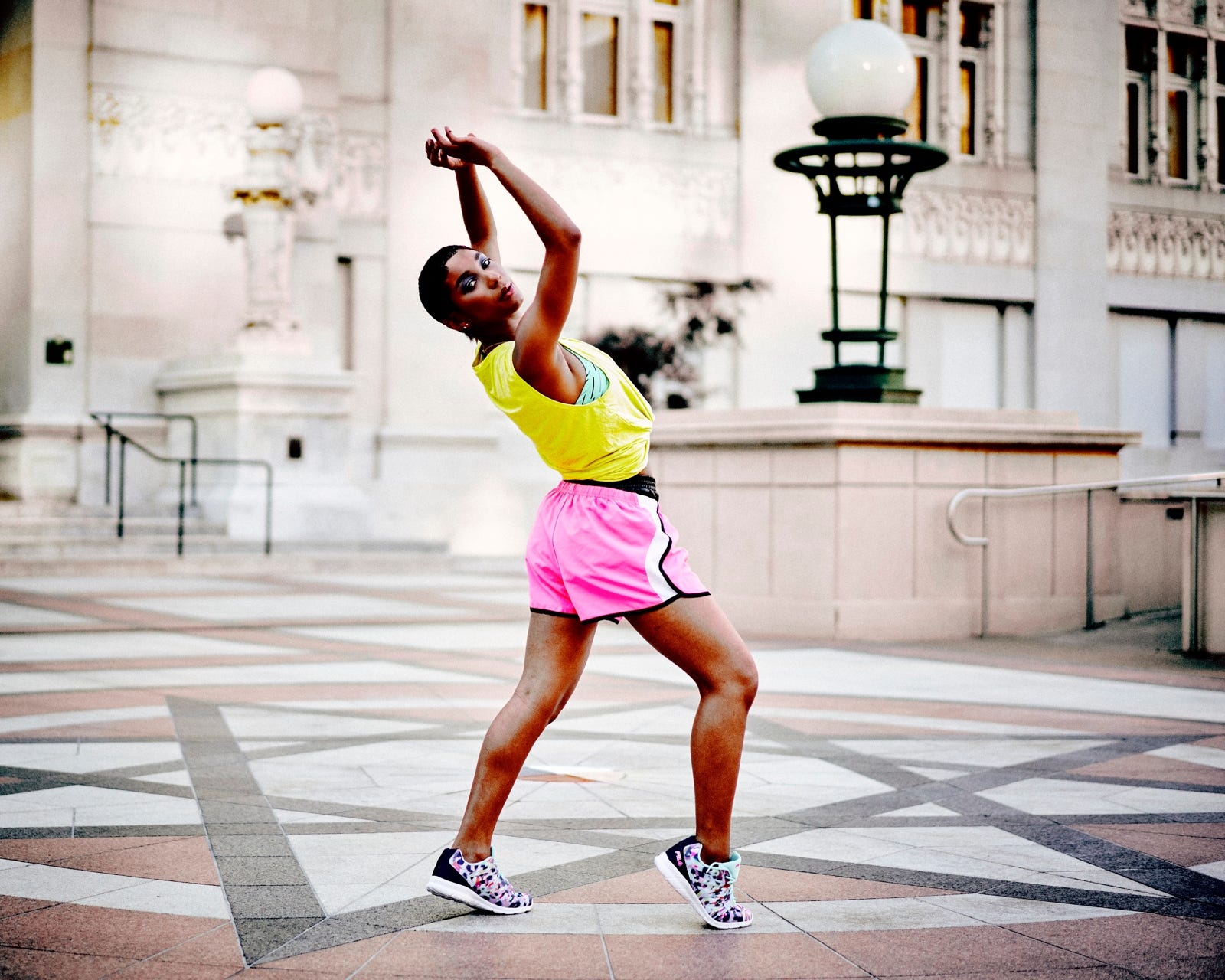 A Black woman with close-shaved hair dancing in front of a neoclassical building or campus hall.