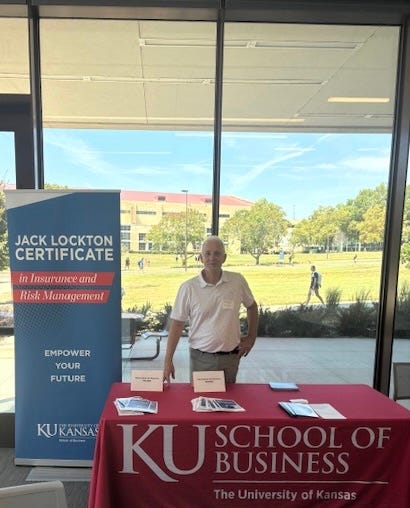 A man stands at a table in front of a glass wall promoting the Jack Locton Certificate.