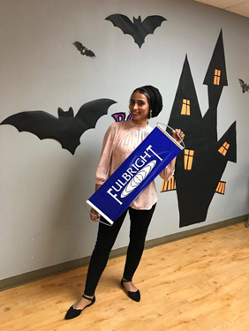 Woman holding a Fulbright sign in front of wall art of bats.