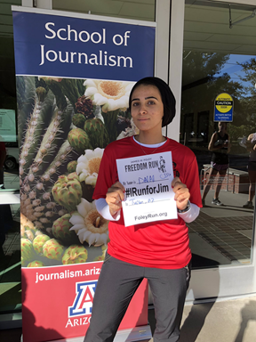 Woman standing next to a School of Journalism banner.