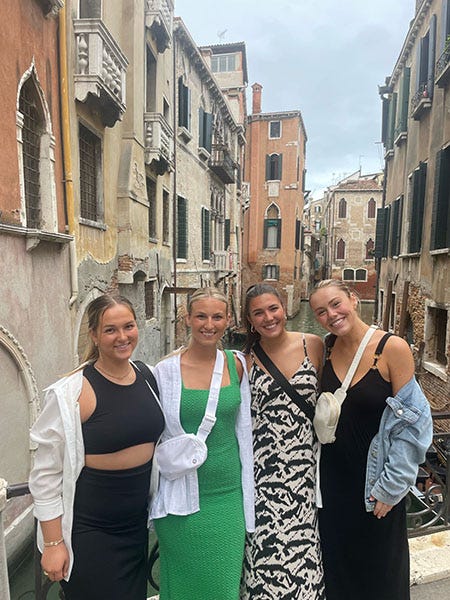 Four women pose for a picture with an Italian canal and buildings in the background.