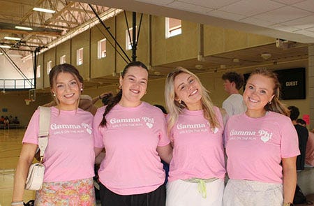 Four women pose for a picture while wearing pink t-shirts that say "Gamma Phi."