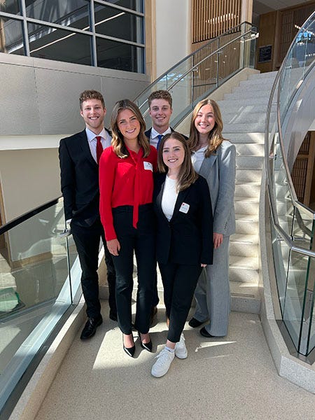 A group of students dressed in business professional clothes pose for a picture on a modern looking staircase.